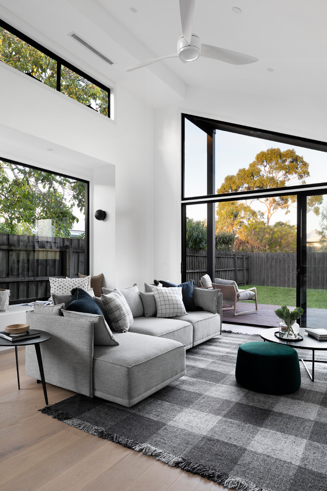 This is an example of a contemporary open concept living room in Melbourne with white walls, light hardwood floors and beige floor.
