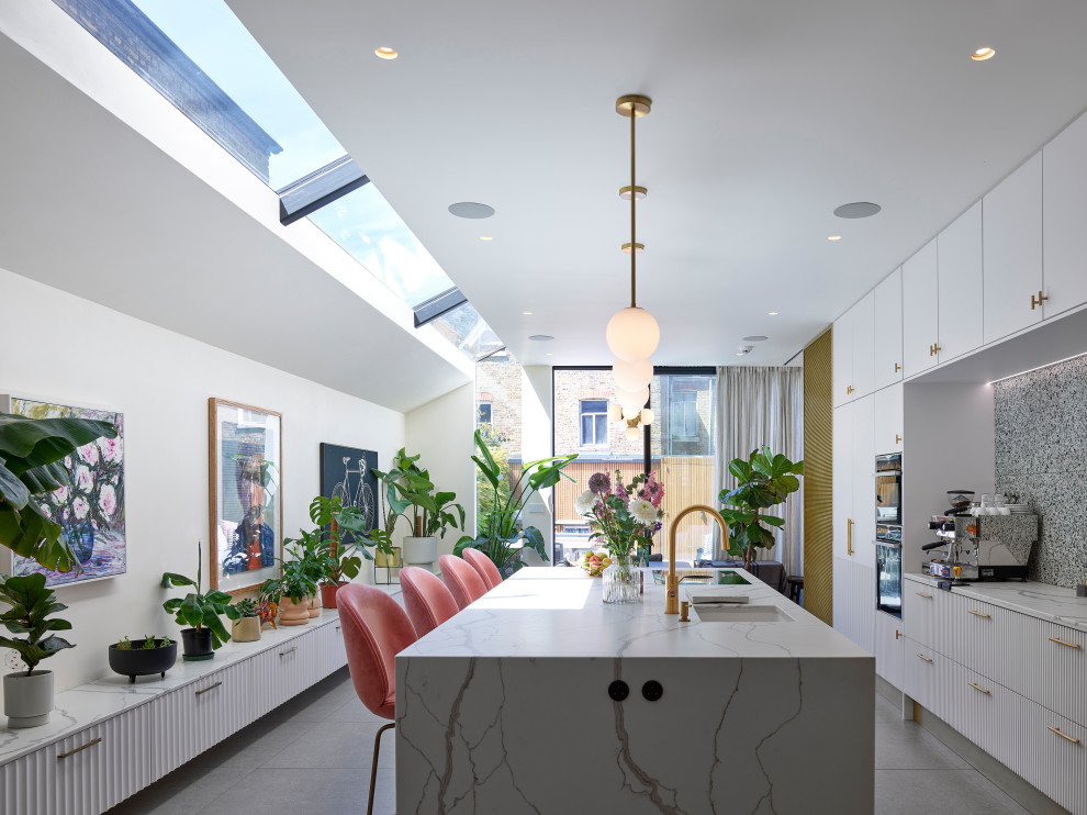 Large contemporary galley kitchen/diner in London with a submerged sink, flat-panel cabinets, white cabinets, composite countertops, travertine splashback, white appliances, ceramic flooring, an island, grey floors, white worktops and feature lighting.