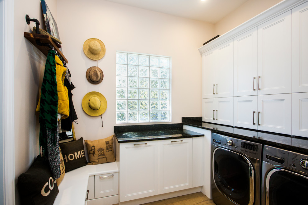This is an example of a mid-sized transitional u-shaped utility room in Tampa with shaker cabinets, white cabinets, granite benchtops, beige walls, medium hardwood floors, a side-by-side washer and dryer, black benchtop and brown floor.