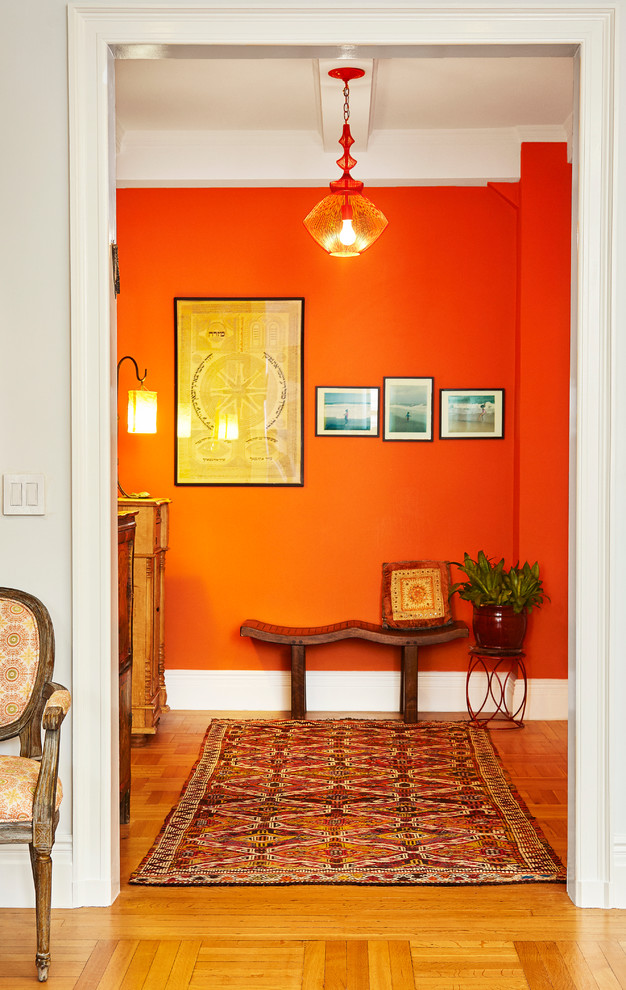 This is an example of a small eclectic foyer in New York with orange walls, light hardwood floors, a single front door and a white front door.