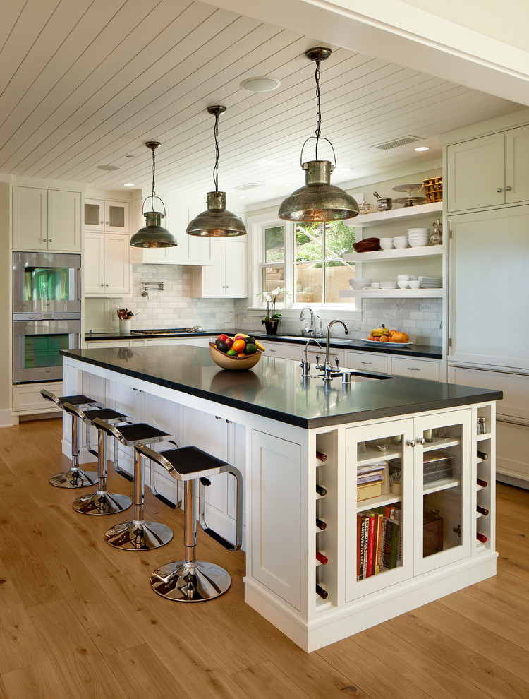 Photo of a large traditional l-shaped kitchen in Santa Barbara with an undermount sink, shaker cabinets, white splashback, panelled appliances, with island, light hardwood floors and black benchtop.