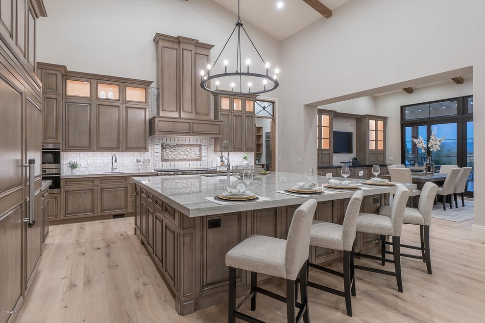 Transitional l-shaped open plan kitchen in Phoenix with a double-bowl sink, recessed-panel cabinets, light wood cabinets, marble benchtops, white splashback, ceramic splashback, panelled appliances, light hardwood floors, with island, beige floor and grey benchtop.