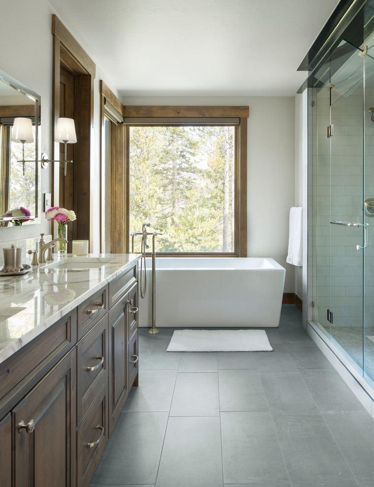 Inspiration for a transitional master bathroom in Denver with raised-panel cabinets, brown cabinets, a freestanding tub, beige tile, white tile, white walls, an undermount sink, grey floor and a hinged shower door.