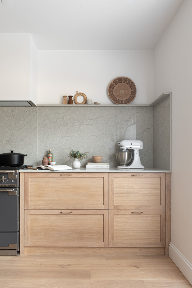This is an example of a large scandinavian grey and cream kitchen/diner in Surrey with an integrated sink, shaker cabinets, light wood cabinets, quartz worktops, grey splashback, black appliances, light hardwood flooring, an island and grey worktops.