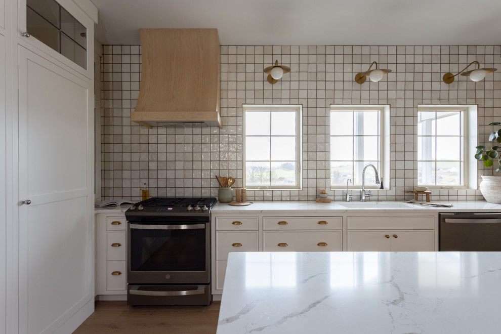 Design ideas for a transitional galley kitchen in Cleveland with an undermount sink, shaker cabinets, white splashback, ceramic splashback, stainless steel appliances, vinyl floors, with island, brown floor and white benchtop.