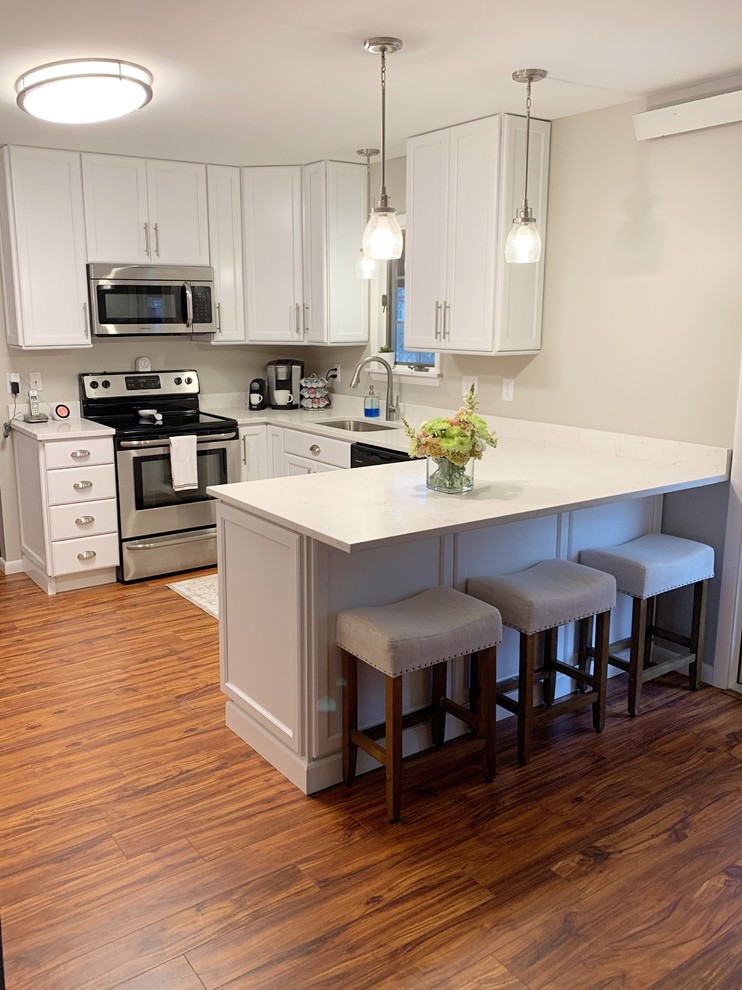 Mid-sized contemporary u-shaped separate kitchen in Burlington with an undermount sink, recessed-panel cabinets, white cabinets, stainless steel appliances, medium hardwood floors, a peninsula, brown floor and white benchtop.