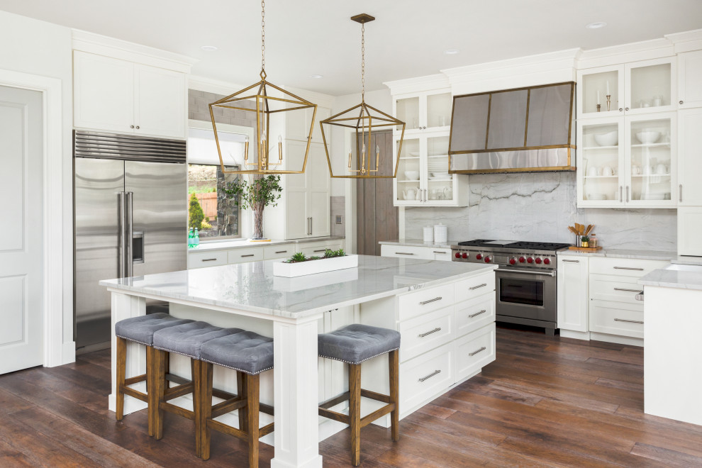 Transitional u-shaped dark wood floor and brown floor kitchen photo with a farmhouse sink, recessed-panel cabinets, white cabinets, gray backsplash, stone slab backsplash, stainless steel appliances, an island and gray countertops