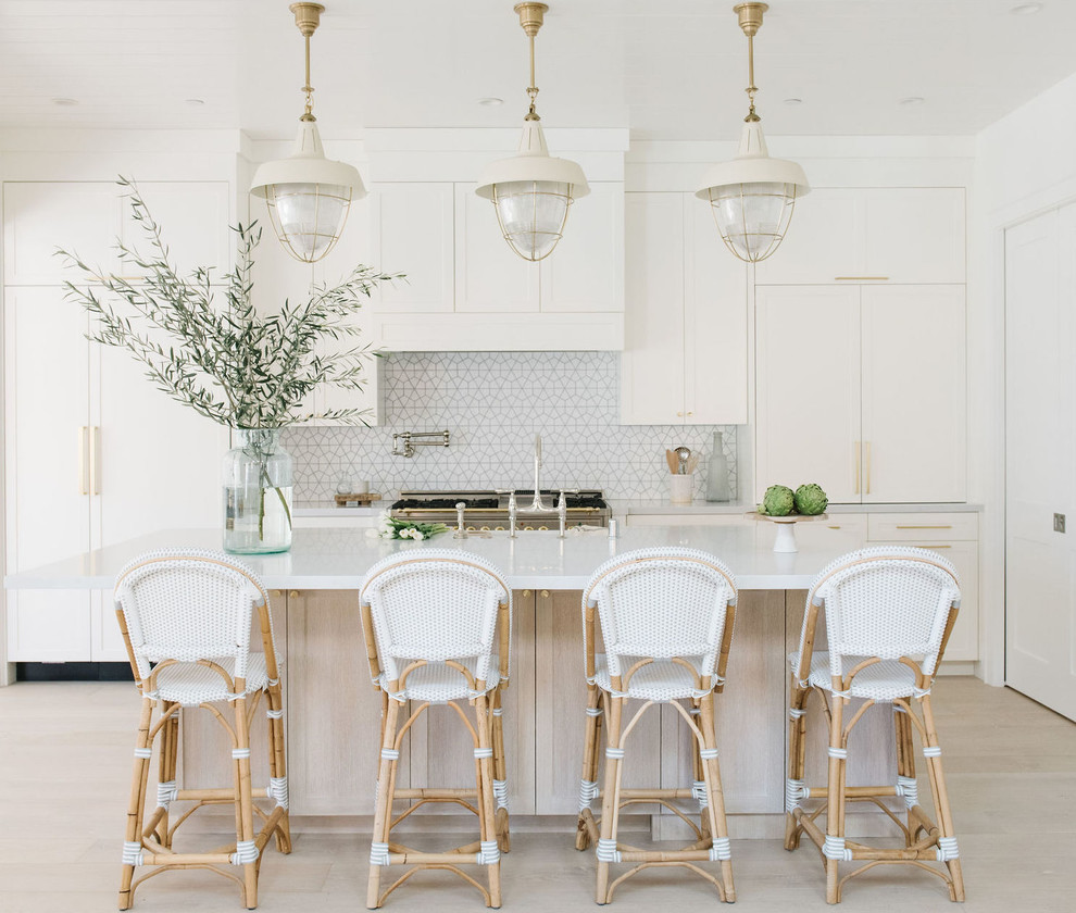 Inspiration for a beach style l-shaped kitchen in San Francisco with recessed-panel cabinets, white cabinets, white splashback, panelled appliances, light hardwood floors, beige floor and white benchtop.