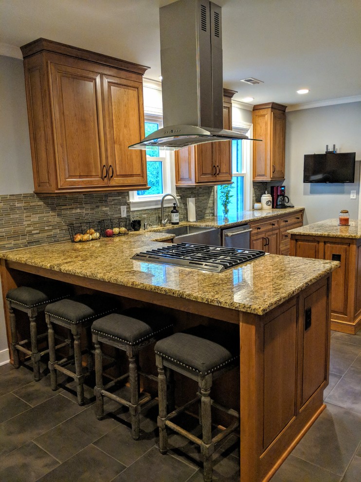 Example of a mid-sized transitional u-shaped porcelain tile and black floor kitchen design with a farmhouse sink, raised-panel cabinets, light wood cabinets, granite countertops, green backsplash, glass sheet backsplash, stainless steel appliances, an island and brown countertops