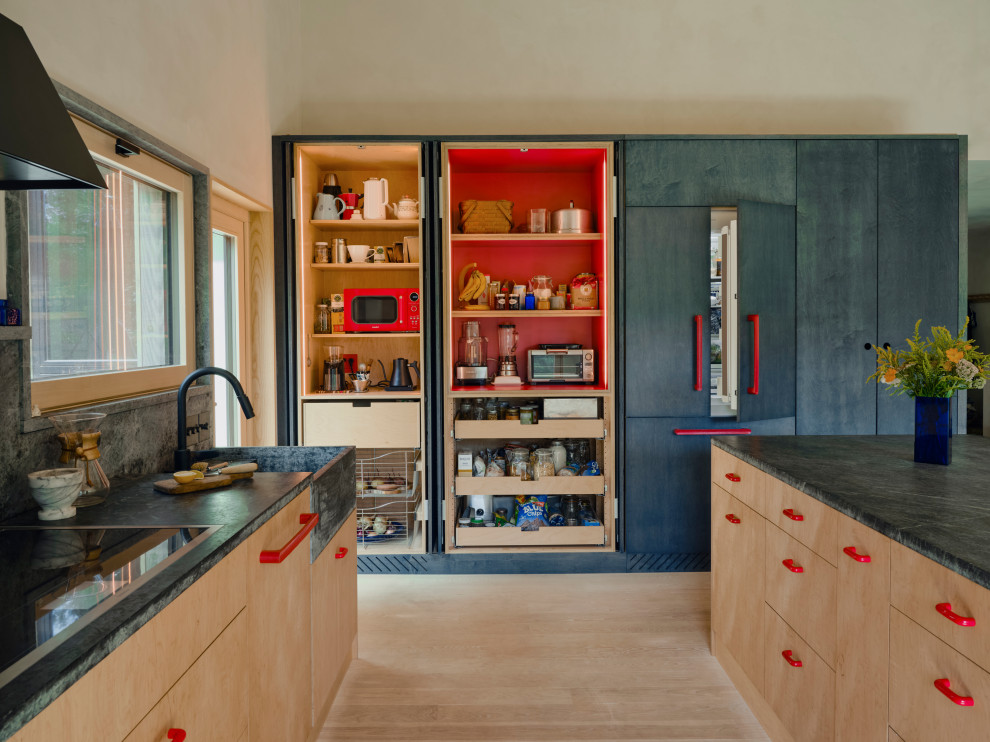 Large danish light wood floor and wood ceiling eat-in kitchen photo in New York with a farmhouse sink, flat-panel cabinets, light wood cabinets, soapstone countertops, gray backsplash, stone slab backsplash, paneled appliances, an island and gray countertops