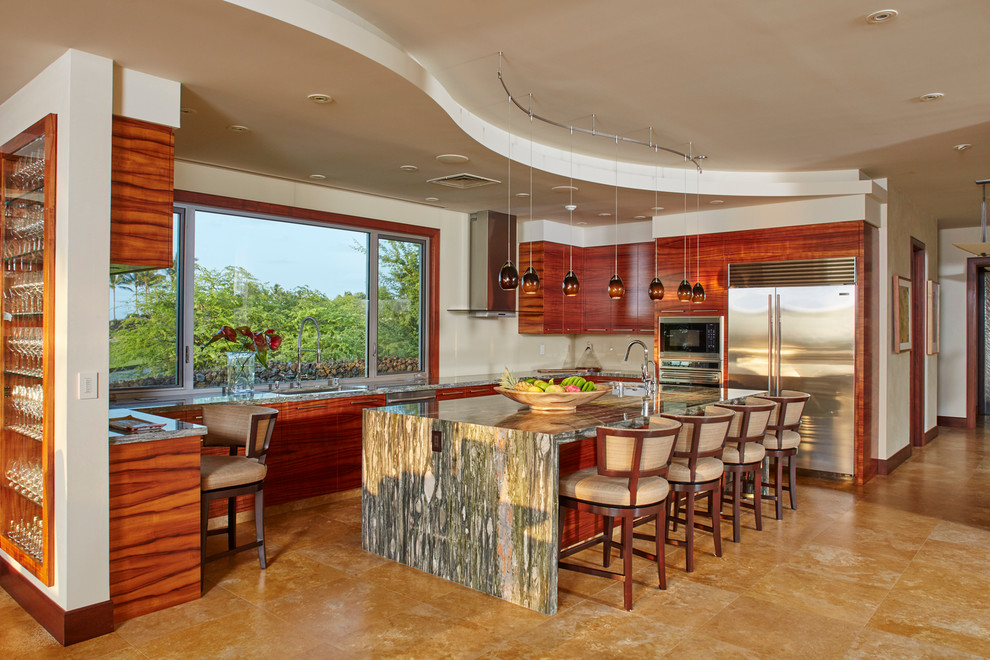 This is an example of a large tropical u-shaped kitchen in Hawaii with an undermount sink, flat-panel cabinets, medium wood cabinets, granite benchtops, stainless steel appliances, travertine floors and with island.