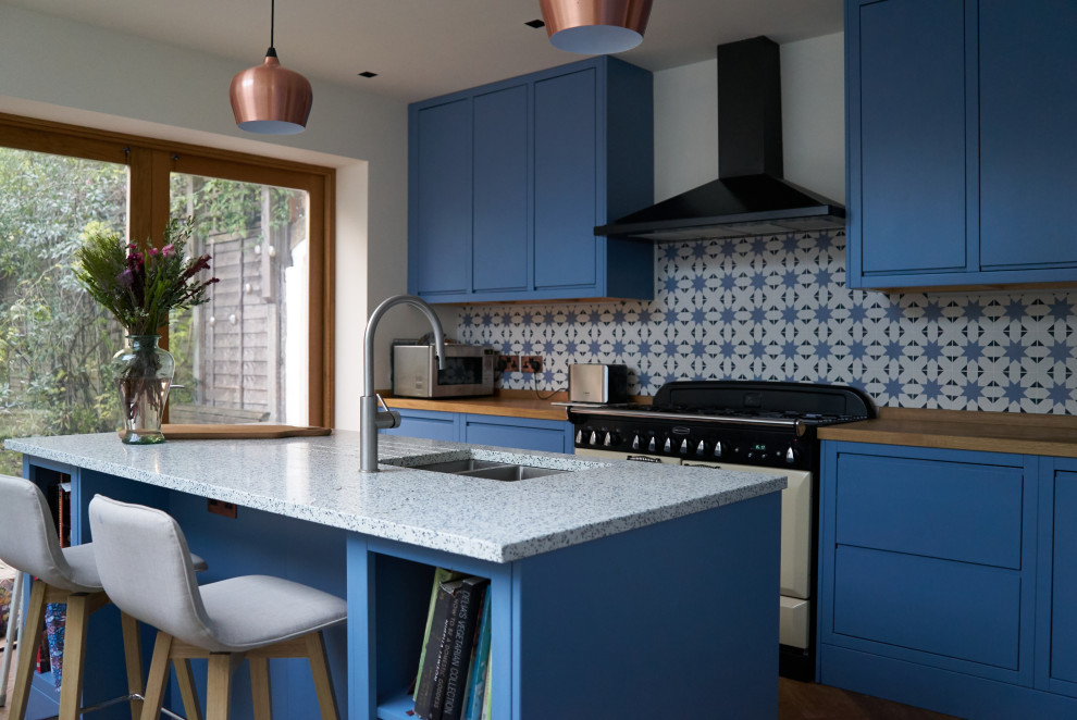 Idéer för att renovera ett stort funkis blå blått kök, med en integrerad diskho, släta luckor, blå skåp, bänkskiva i återvunnet glas, blått stänkskydd, stänkskydd i porslinskakel, vita vitvaror, ljust trägolv och en köksö