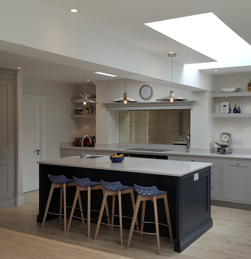 This is an example of a contemporary l-shaped eat-in kitchen in Dublin with a drop-in sink, recessed-panel cabinets, marble benchtops, metallic splashback, mirror splashback, panelled appliances, porcelain floors and with island.