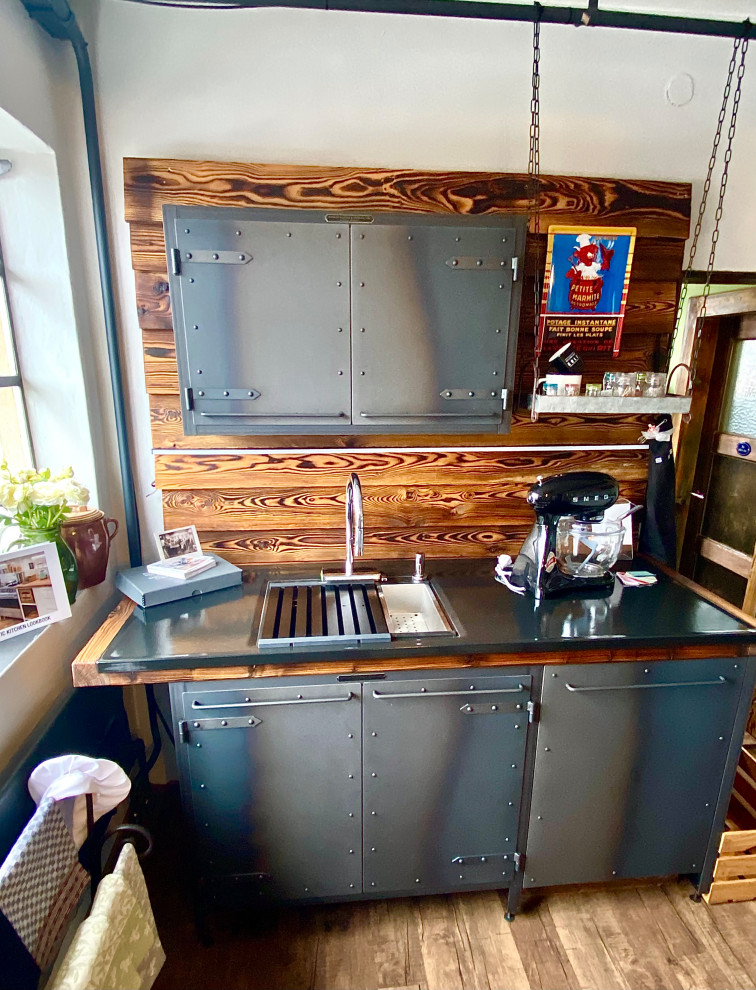 Mid-sized urban single-wall linoleum floor and brown floor open concept kitchen photo in Munich with a single-bowl sink, stainless steel cabinets, solid surface countertops, wood backsplash, no island and black countertops