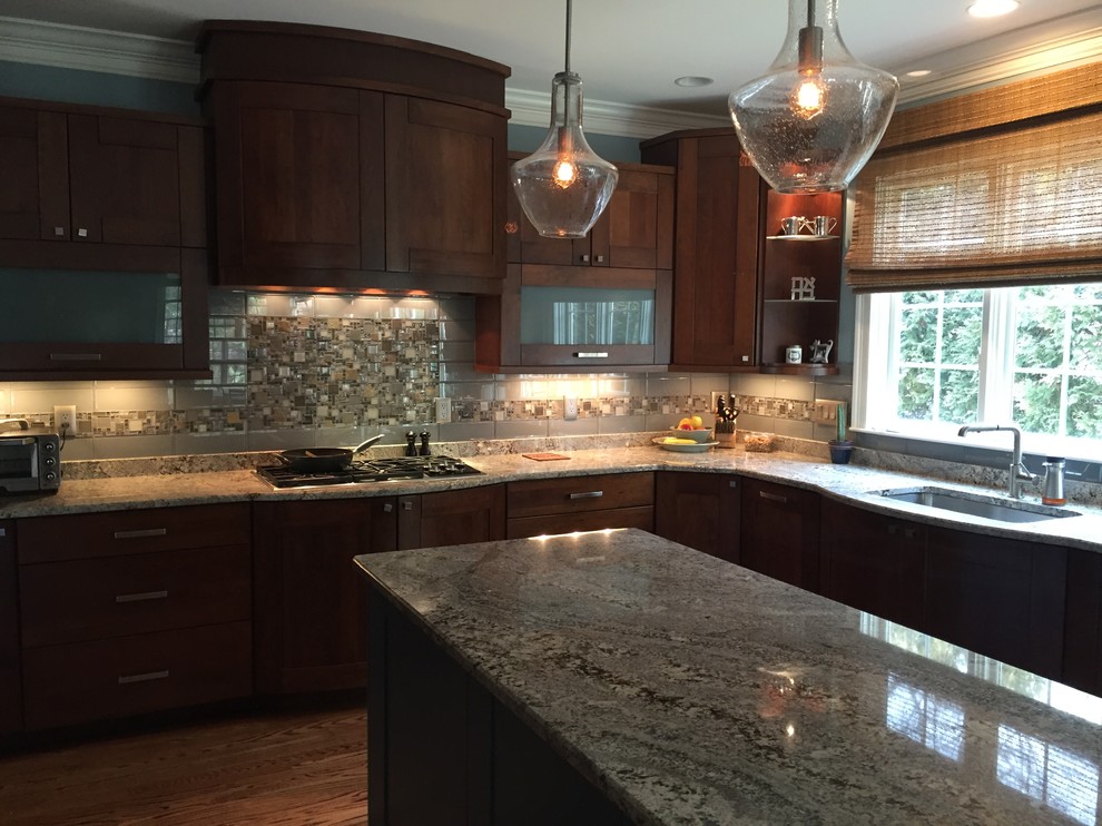Example of a large transitional l-shaped medium tone wood floor open concept kitchen design with a single-bowl sink, glass-front cabinets, dark wood cabinets, granite countertops, gray backsplash, glass tile backsplash, stainless steel appliances and an island