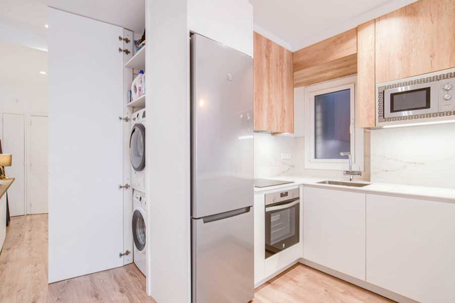 Inspiration for a small scandinavian single-wall laundry cupboard in Barcelona with an undermount sink, flat-panel cabinets, white cabinets, quartz benchtops, white splashback, marble splashback, white walls, medium hardwood floors, a stacked washer and dryer, brown floor and white benchtop.