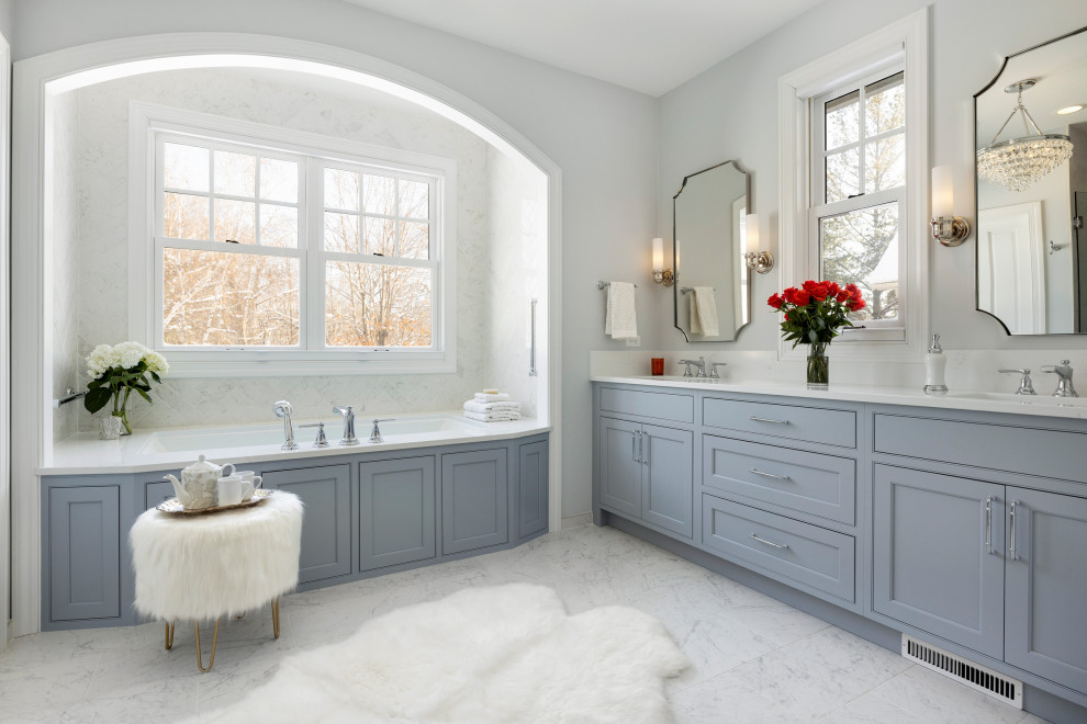 Design ideas for an ensuite bathroom in Minneapolis with recessed-panel cabinets, blue cabinets, a submerged bath, an alcove shower, a two-piece toilet, white tiles, marble tiles, grey walls, marble flooring, a submerged sink, engineered stone worktops, white floors, a hinged door, white worktops, a shower bench, double sinks and a built in vanity unit.