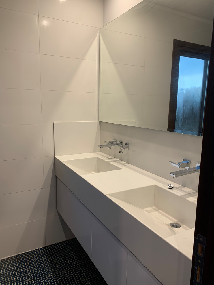 Photo of a mid-sized contemporary kids bathroom in Other with flat-panel cabinets, white cabinets, a drop-in tub, a shower/bathtub combo, a two-piece toilet, blue tile, mosaic tile, white walls, mosaic tile floors, an integrated sink, engineered quartz benchtops, blue floor, a sliding shower screen, white benchtops, a shower seat, a double vanity and a built-in vanity.