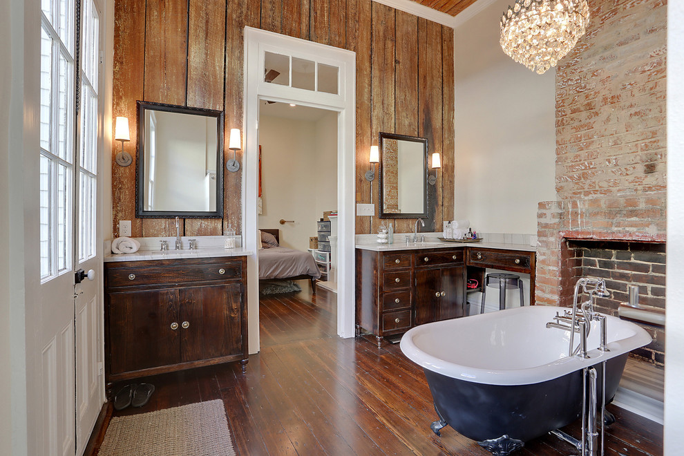 Photo of a mid-sized country master bathroom in New Orleans with dark wood cabinets, a claw-foot tub, flat-panel cabinets, brown tile, beige walls, medium hardwood floors, an undermount sink, engineered quartz benchtops, brown floor and white benchtops.
