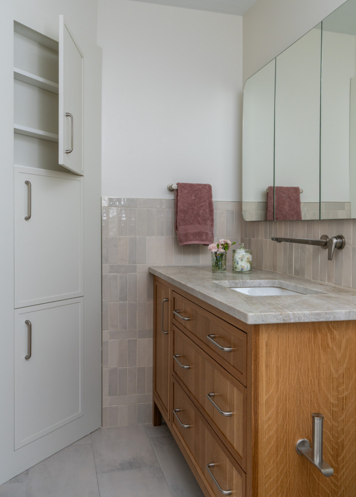 Mid-sized minimalist kids' beige tile and cement tile porcelain tile, beige floor and single-sink drop-in bathtub photo in Minneapolis with recessed-panel cabinets, light wood cabinets, a one-piece toilet, white walls, an undermount sink, marble countertops, beige countertops and a freestanding vanity