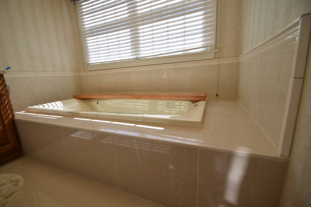 Example of a mid-sized transitional master beige tile and porcelain tile porcelain tile and gray floor drop-in bathtub design with raised-panel cabinets, medium tone wood cabinets, a one-piece toilet, blue walls, an undermount sink, marble countertops and multicolored countertops