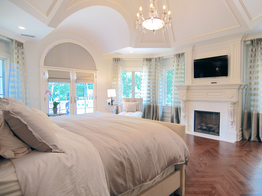 This is an example of a large traditional master bedroom in New York with grey walls, medium hardwood floors, a standard fireplace, a wood fireplace surround and brown floor.