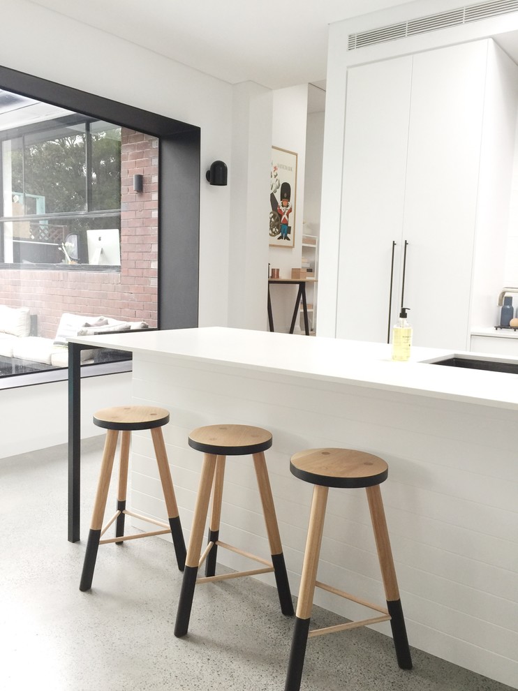 Design ideas for a large scandinavian open plan kitchen in Sydney with an undermount sink, white cabinets, solid surface benchtops, white splashback, ceramic splashback, stainless steel appliances, concrete floors, with island and grey floor.