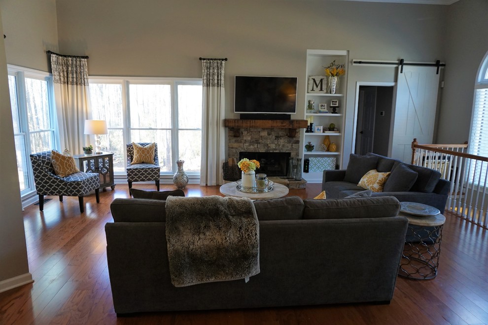 Photo of a mid-sized transitional open concept family room in Atlanta with grey walls, medium hardwood floors, a standard fireplace, a stone fireplace surround, a wall-mounted tv and red floor.