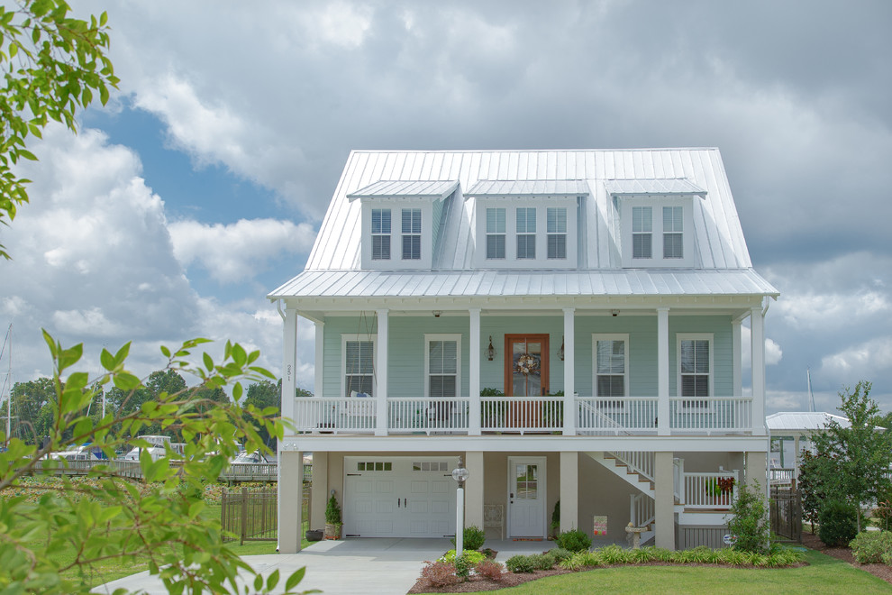Photo of a large beach style three-storey blue house exterior in Raleigh with concrete fiberboard siding, a gable roof and a metal roof.