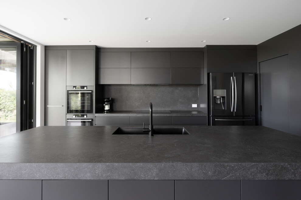 Inspiration for a mid-sized contemporary galley open plan kitchen in Sydney with an undermount sink, grey cabinets, solid surface benchtops, grey splashback, stone slab splashback, black appliances, cement tiles, with island, grey floor and grey benchtop.
