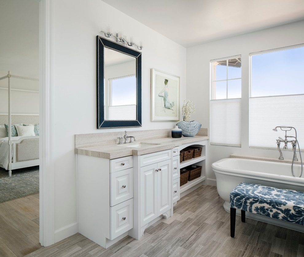 Large beach style master bathroom in San Francisco with raised-panel cabinets, white cabinets, a freestanding tub, gray tile, white walls, an undermount sink, a two-piece toilet, porcelain tile, light hardwood floors, wood benchtops and beige benchtops.