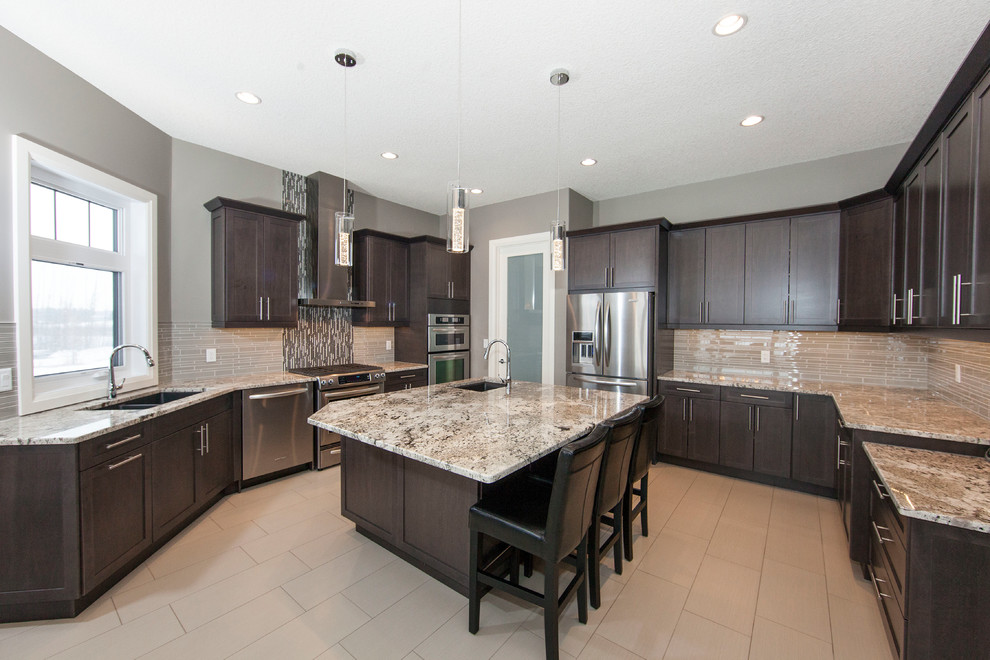 Photo of a large contemporary u-shaped eat-in kitchen in Edmonton with a double-bowl sink, recessed-panel cabinets, dark wood cabinets, granite benchtops, beige splashback, glass tile splashback, stainless steel appliances, ceramic floors and with island.