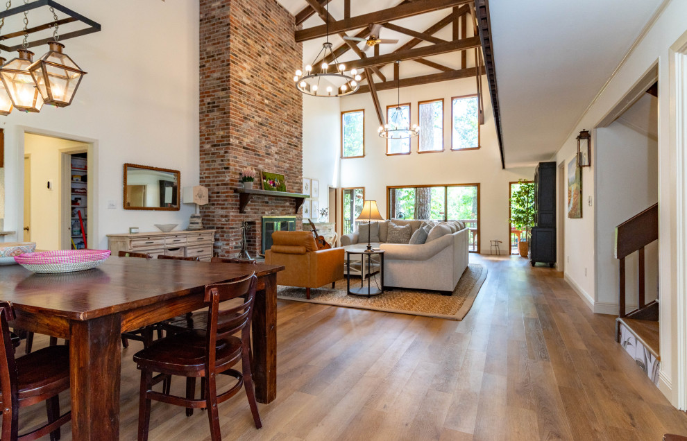 Photo of a large country formal open concept living room in New Orleans with white walls, vinyl floors, a standard fireplace, a brick fireplace surround, brown floor and exposed beam.