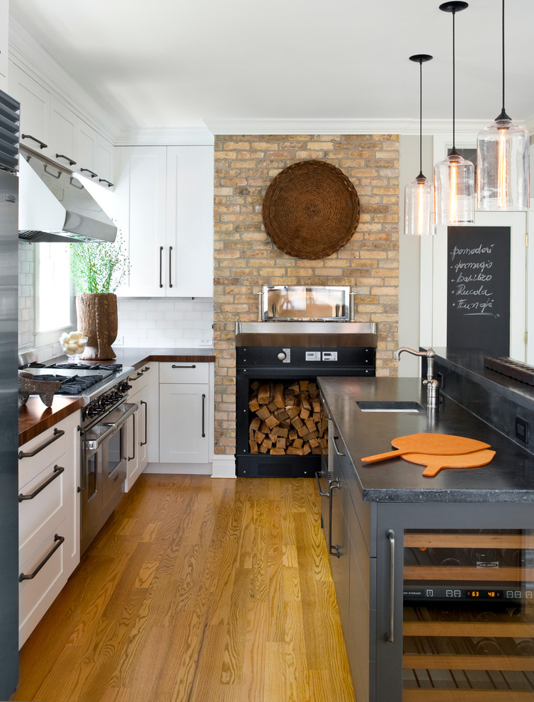 Design ideas for a mid-sized transitional l-shaped kitchen in Chicago with a single-bowl sink, shaker cabinets, white cabinets, white splashback, subway tile splashback, stainless steel appliances, medium hardwood floors, with island and wood benchtops.