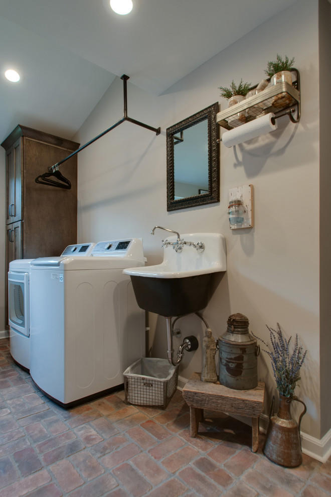 Design ideas for a small country utility room in Nashville with a farmhouse sink, shaker cabinets, brown cabinets, granite benchtops, grey walls, brick floors, a side-by-side washer and dryer, multi-coloured floor and black benchtop.