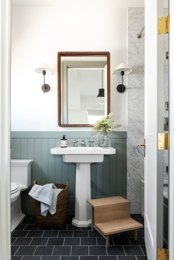 На фото: ванная комната в стиле неоклассика (современная классика) с серой плиткой, белыми стенами, раковиной с пьедесталом, черным полом, тумбой под одну раковину и панелями на стенах с