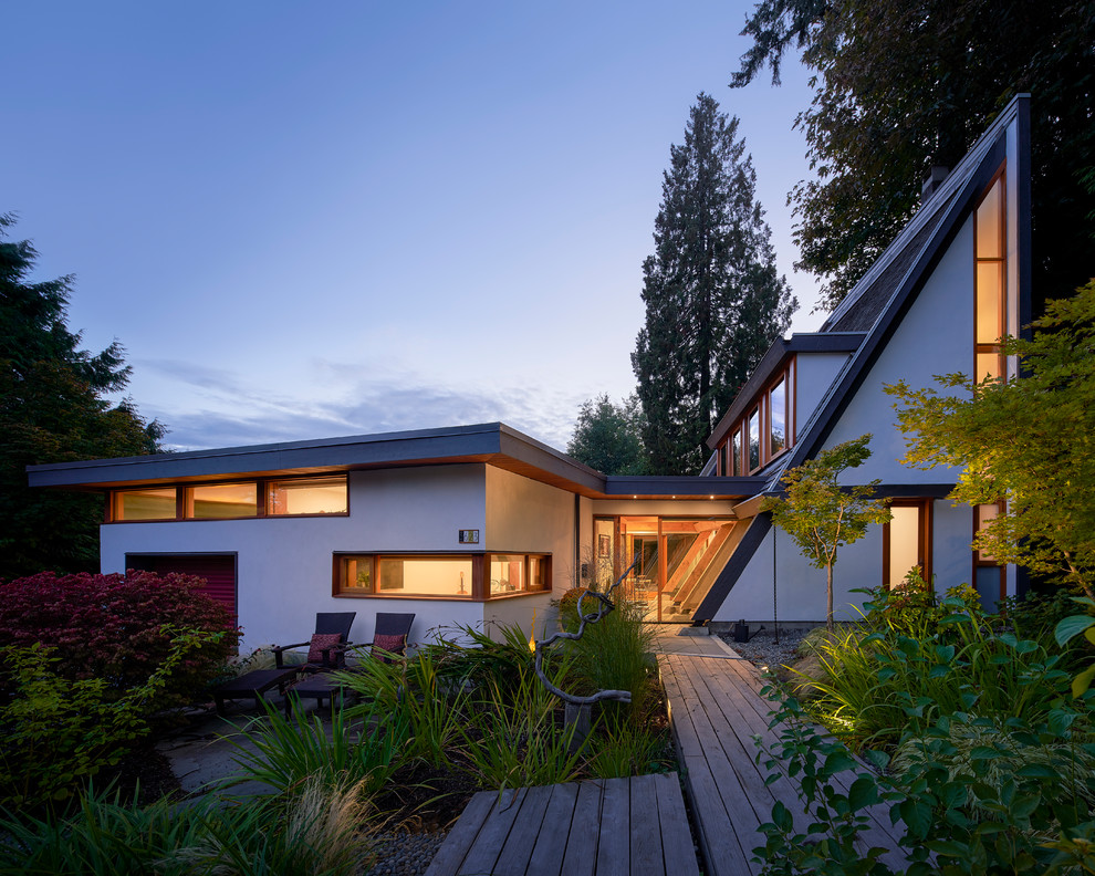 This is an example of a large midcentury two-storey stucco white house exterior in Vancouver with a shingle roof.