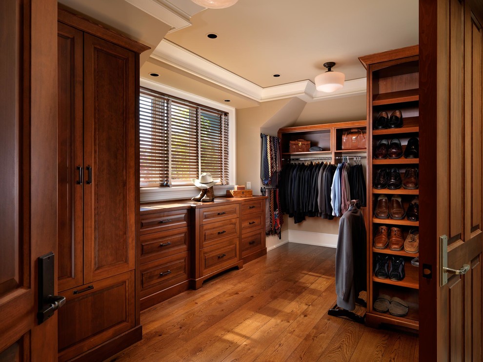Expansive arts and crafts men's walk-in wardrobe in Vancouver with dark wood cabinets and dark hardwood floors.