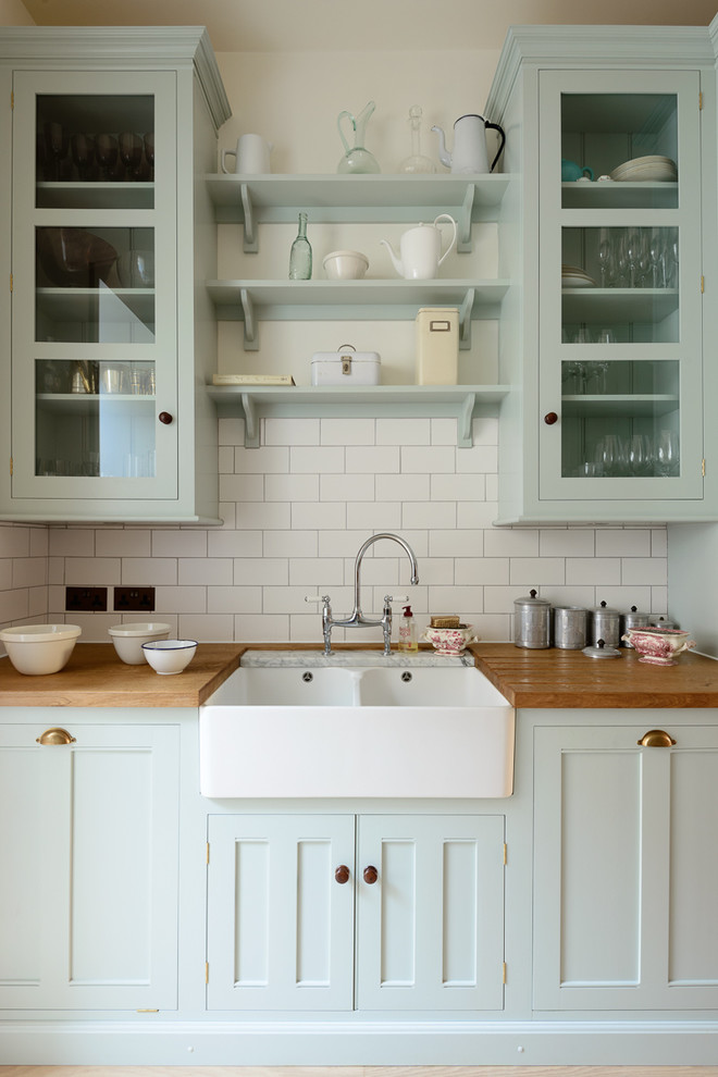 Design ideas for a mid-sized traditional single-wall separate kitchen in London with beaded inset cabinets, blue cabinets, wood benchtops, white splashback, subway tile splashback, stainless steel appliances, light hardwood floors, no island and a double-bowl sink.