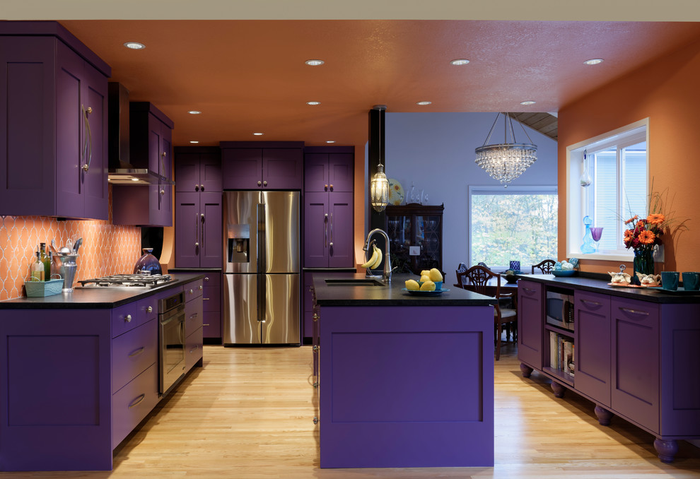 This is an example of a large eclectic galley eat-in kitchen in Portland with an undermount sink, shaker cabinets, purple cabinets, solid surface benchtops, orange splashback, ceramic splashback, stainless steel appliances, light hardwood floors and with island.