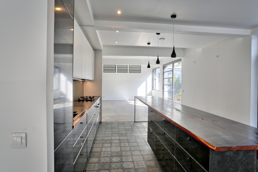 Large contemporary galley open plan kitchen in Paris with an undermount sink, flat-panel cabinets, black cabinets, wood benchtops, beige splashback, mosaic tile splashback, ceramic floors, with island, grey floor, stainless steel appliances and red benchtop.