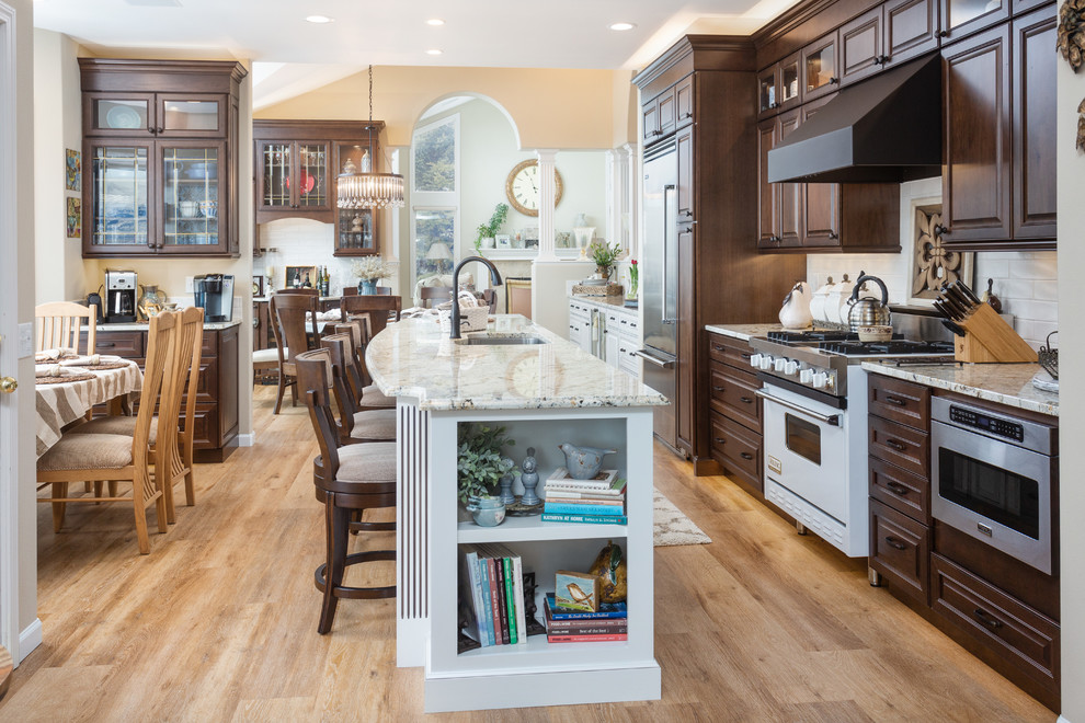 Photo of an expansive traditional galley eat-in kitchen in Other with a single-bowl sink, raised-panel cabinets, dark wood cabinets, granite benchtops, white splashback, ceramic splashback, stainless steel appliances, vinyl floors, with island, beige floor and beige benchtop.
