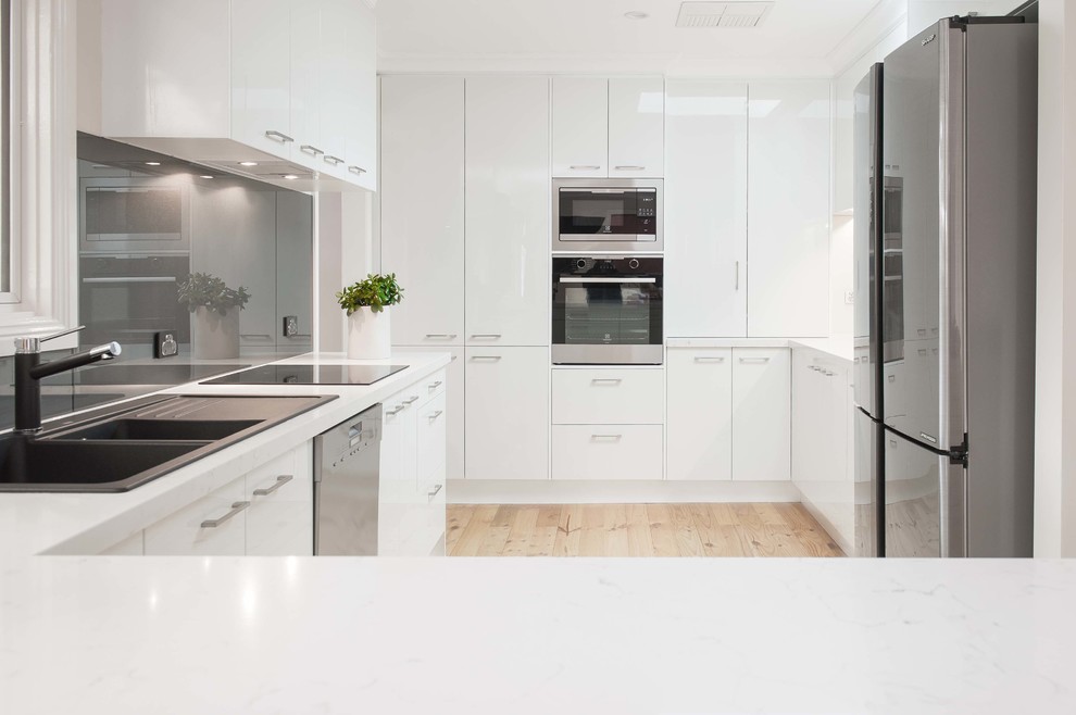 Mid-sized contemporary u-shaped kitchen pantry in Melbourne with a double-bowl sink, open cabinets, white cabinets, solid surface benchtops, metallic splashback, glass sheet splashback, stainless steel appliances, light hardwood floors, with island and beige floor.