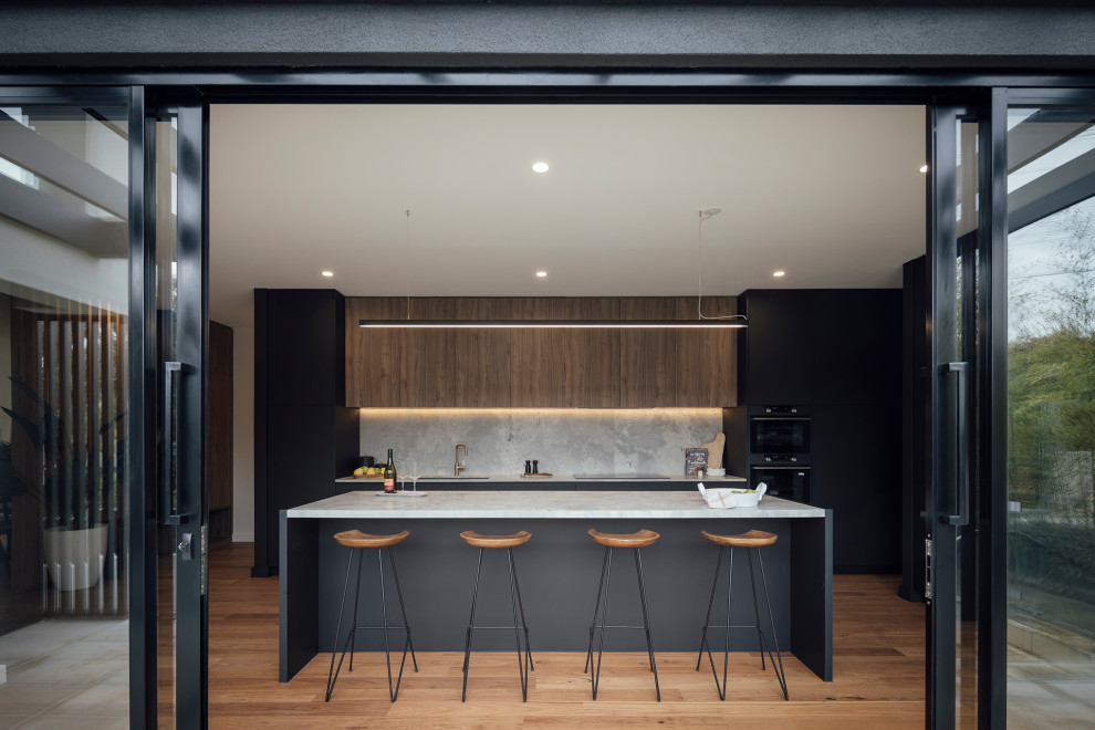 Aménagement d'une cuisine parallèle contemporaine de taille moyenne avec un plan de travail en surface solide, un électroménager noir, un sol en bois brun et îlot.