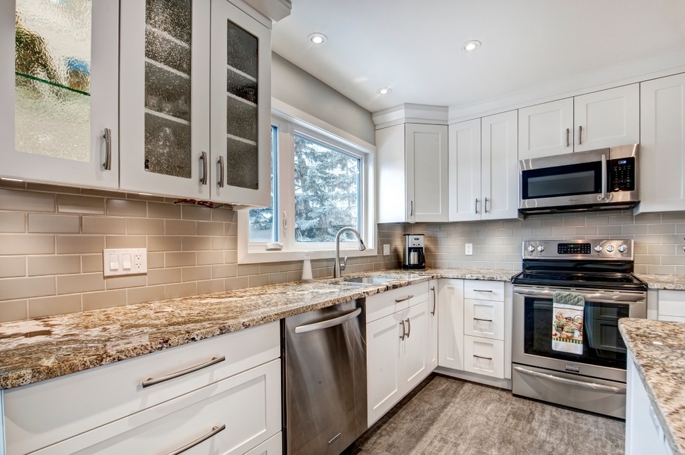 Mid-sized transitional l-shaped eat-in kitchen in Calgary with an undermount sink, shaker cabinets, white cabinets, granite benchtops, grey splashback, subway tile splashback, stainless steel appliances, vinyl floors and with island.