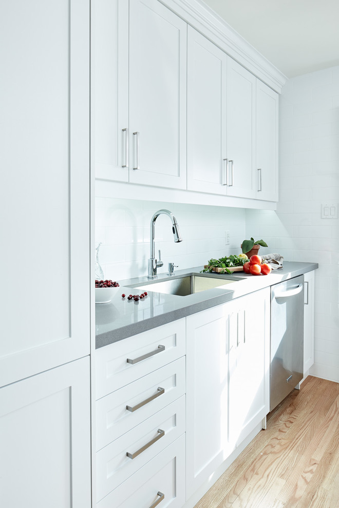 Inspiration for a small modern galley separate kitchen in Toronto with an undermount sink, shaker cabinets, white cabinets, quartz benchtops, white splashback, porcelain splashback, stainless steel appliances, light hardwood floors and no island.