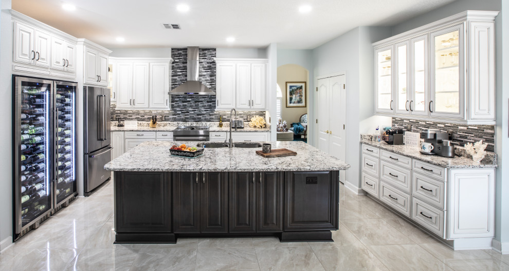 Photo of a large transitional u-shaped eat-in kitchen in Orlando with a double-bowl sink, raised-panel cabinets, white cabinets, quartz benchtops, metallic splashback, mosaic tile splashback, porcelain floors, with island, beige floor and beige benchtop.