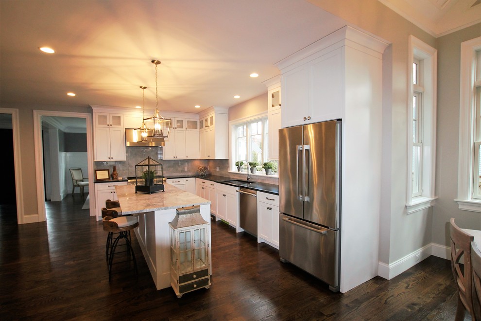 Large transitional l-shaped dark wood floor and brown floor eat-in kitchen photo in Boston with an undermount sink, shaker cabinets, white cabinets, granite countertops, beige backsplash, marble backsplash, stainless steel appliances and an island