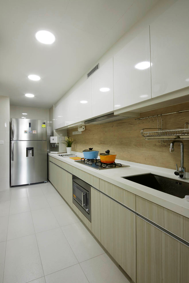 Photo of a mid-sized modern galley kitchen in Singapore with a drop-in sink, flat-panel cabinets, light wood cabinets, solid surface benchtops, brown splashback, stainless steel appliances and ceramic floors.