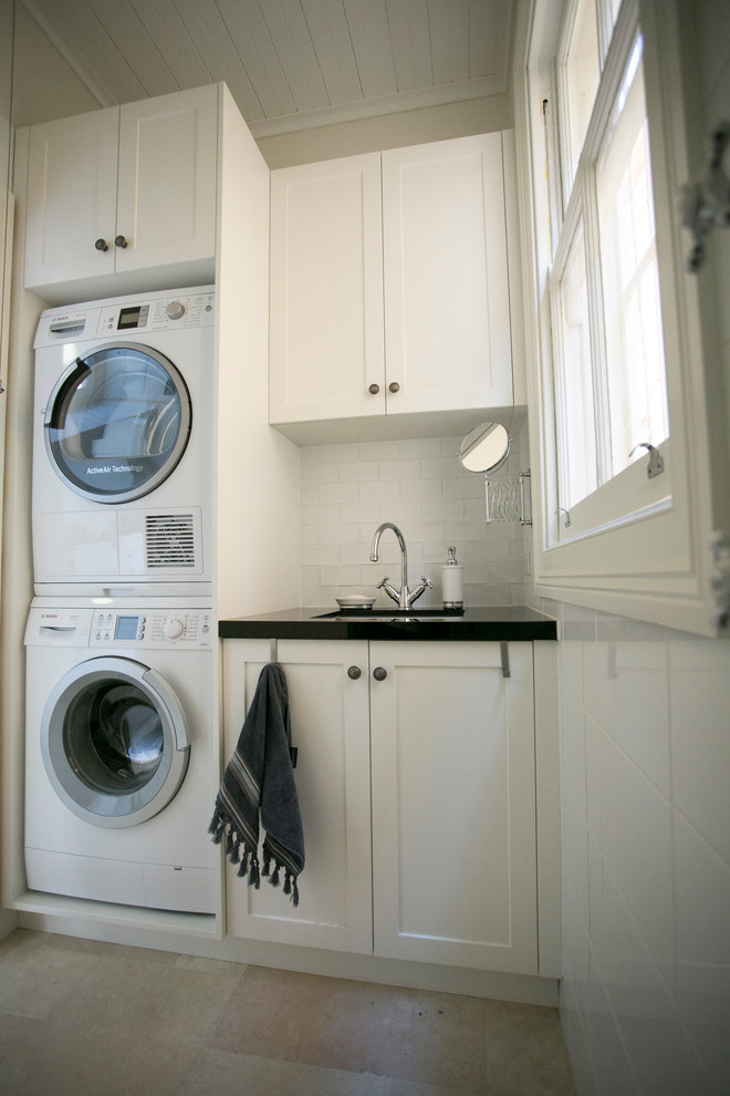 Inspiration for a small traditional single-wall dedicated laundry room in Sydney with shaker cabinets, white cabinets, white walls, limestone floors and a stacked washer and dryer.